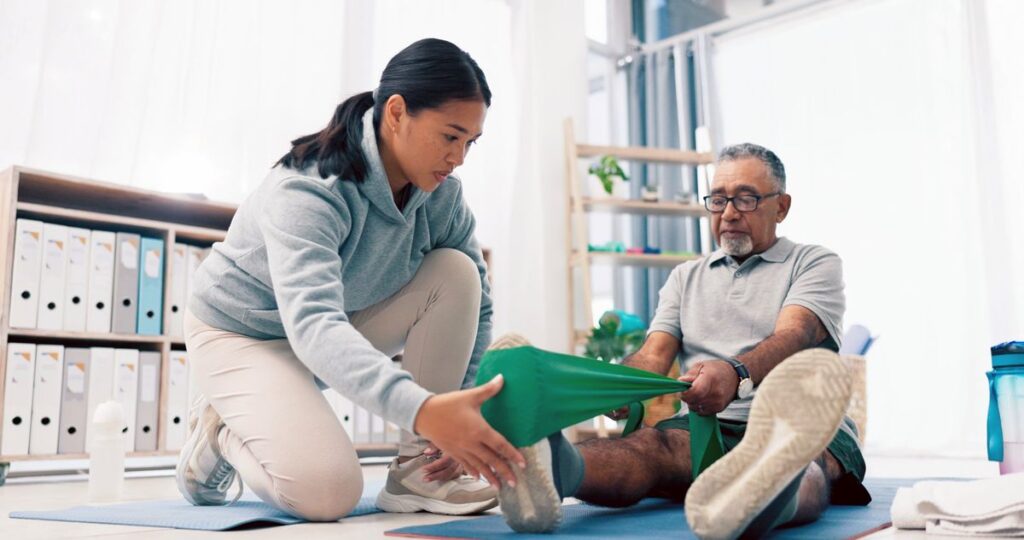 Young Asian female physiotherapist treating man's leg
