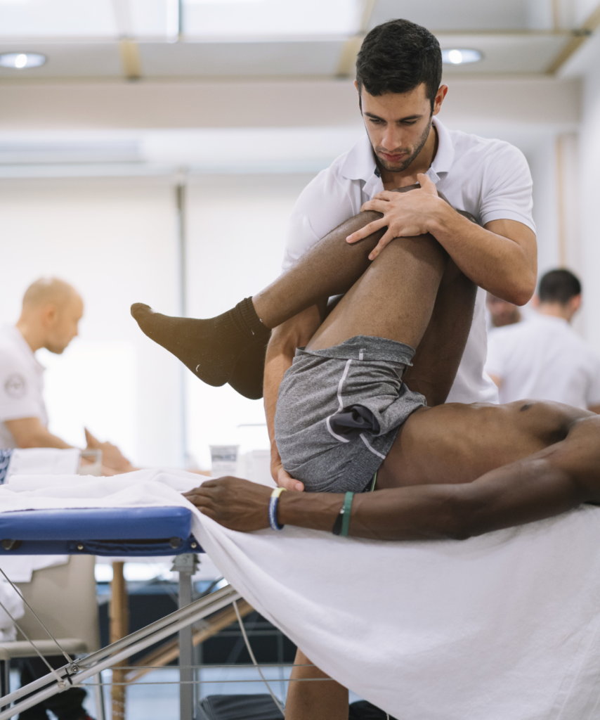 Male physiotherapist treating client who is lying down and his knees are up and being held by PT